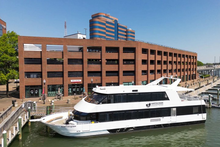 White boat docked by a brick building with tables and chairs outside.